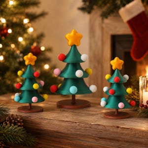 Könnte beinhalten: Drei dekorative Tisch-Weihnachtsbäume in verschiedenen Größen, jeweils mit einer dunkelgrünen Kegelform, einem braunen runden Sockel und einem gelben Stern als Spitze. Die Bäume sind mit kleinen, bunten, kugelförmigen Ornamenten in Rot, Weiß, Gelb, Rosa und Hellblau verziert.