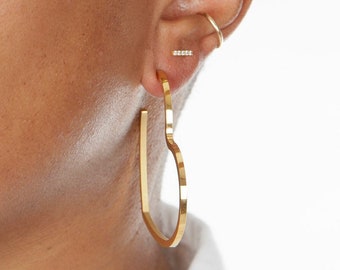 May include: Gold heart-shaped hoop earrings. The earrings are made of a thick, solid gold wire and have a smooth, polished finish.