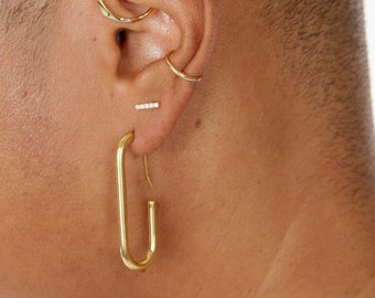 May include: A person's ear with multiple gold earrings. The earrings include a hoop, a small stud, a bar with small diamonds, and a large oval hoop.