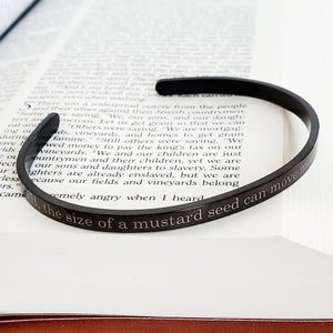 May include: A black metal bracelet with an engraved quote: "Faith the size of a mustard seed can move mountains".