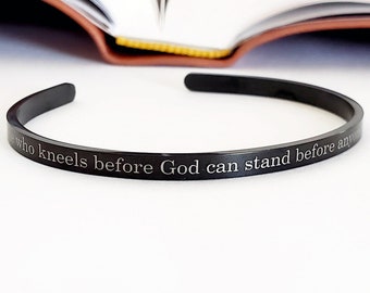 May include: A black metal bangle bracelet with the inscription "Only who kneels before God can stand before anyone".