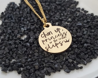 May include: Gold necklace with a round pendant that says "Chin up, princess or the crown slips" with a crown symbol.
