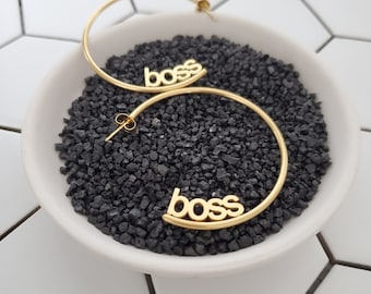 May include: A pair of gold hoop earrings with the word "boss" spelled out on each hoop.