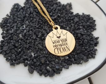 May include: Gold necklace with a round pendant that says "Wear your invisible crown" with a small heart above the word "your".