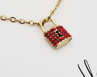 May include: Gold necklace with a red crystal-encrusted padlock pendant.