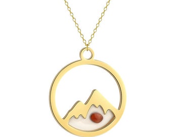 May include: A gold necklace with a circular pendant featuring a mountain silhouette and a small red gemstone. The pendant is open in the center, revealing a white background.