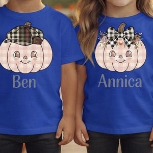 Könnte beinhalten: Zwei königsblaue T-Shirts mit einer hellrosa karierten Kürbisgrafik. Das linke T-Shirt zeigt einen Kürbis mit einer schwarz-weiß karierten Mütze und dem Namen Ben. Das rechte T-Shirt zeigt einen Kürbis mit einer karierten Schleife und dem Namen Annica.