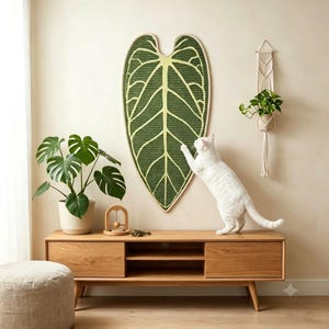 Puede incluir: Un rascador para gatos grande en forma de corazón montado en la pared, con un diseño de hoja verde oscuro y venas verde claro. La superficie texturizada está diseñada para las garras y se fija sobre un mueble multimedia de madera.