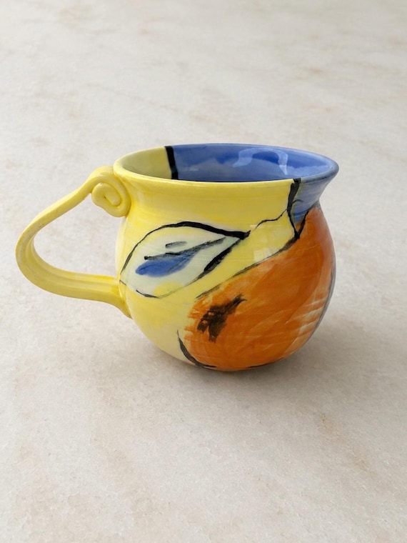 A hand-painted pear ceramic mug with a Mediterranean folk-art feel — the kind of artisan piece that makes your morning coffee feel like a tiny vacation to an Italian market.