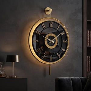 Op de afbeelding: Een ronde wandklok met een zwarte wijzerplaat en goudkleurige cijfers en wijzers. De klok heeft een goudkleurige rand met een geïntegreerde lichtring, een verticale bevestigingsstang en een dunne, rechte slinger aan de onderkant.
