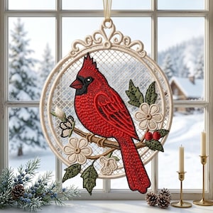 May include: A circular hanging ornament featuring intricate embroidery of a bright red cardinal bird perched on a brown branch. The design includes cream-colored flowers, green leaves, and small red berries, all set within a cream-colored lattice frame.