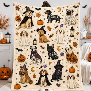Peut inclure: Une couverture en polaire crème ornée d'un motif répétitif de diverses races de chiens déguisés pour Halloween, incluant des fantômes, des squelettes et des sorcières, parsemée d'illustrations de citrouilles, chauves-souris, étoiles et lunes.