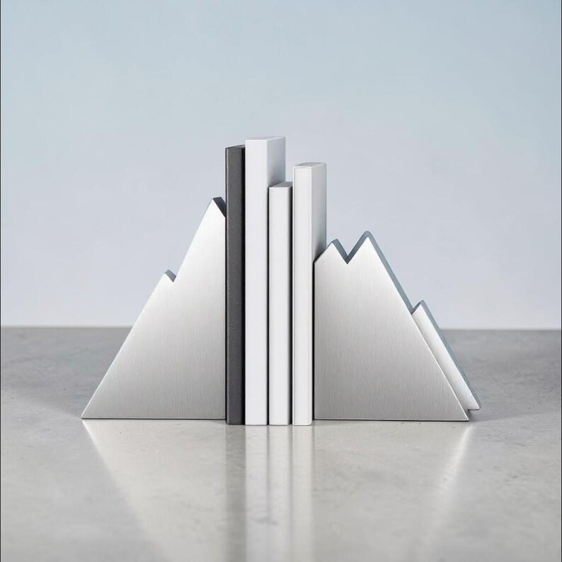 Peut inclure: Une paire de serre-livres en m&eacute;tal argent&eacute; en forme de sommets montagneux, maintenant trois livres &agrave; la verticale. Les serre-livres pr&eacute;sentent une finition bross&eacute;e, et les livres se composent d'un dos noir et de deux dos blancs align&eacute;s.