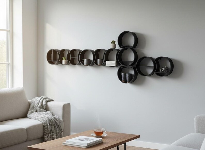 May include: A wall-mounted shelving unit composed of multiple interconnected black circular frames of varying sizes. The shelves hold small potted plants, ceramic mugs, and a stack of books, creating a modular storage display on the wall.