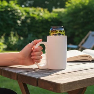 May include: A plain white cylindrical mug with a large, ergonomic handle designed to hold a standard beverage can. The mug is matte white and features a wide opening at the top, allowing a black and yellow can labeled Lando Norris to sit inside.