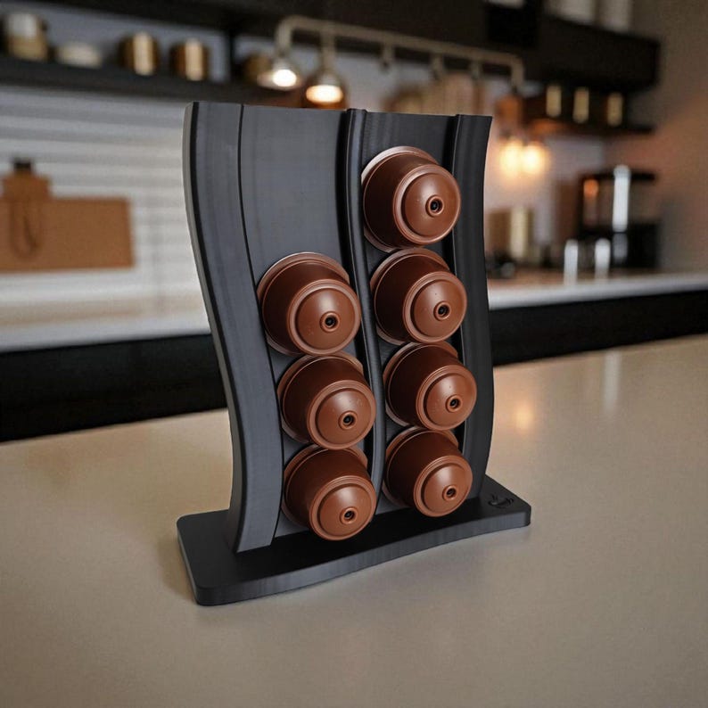Puede incluir: Un soporte vertical negro para c&aacute;psulas de caf&eacute; con dise&ntilde;o ondulado, que cuenta con dos columnas para un total de ocho c&aacute;psulas de caf&eacute; marrones. El soporte tiene una base rectangular y un acabado liso y mate para almacenamiento.