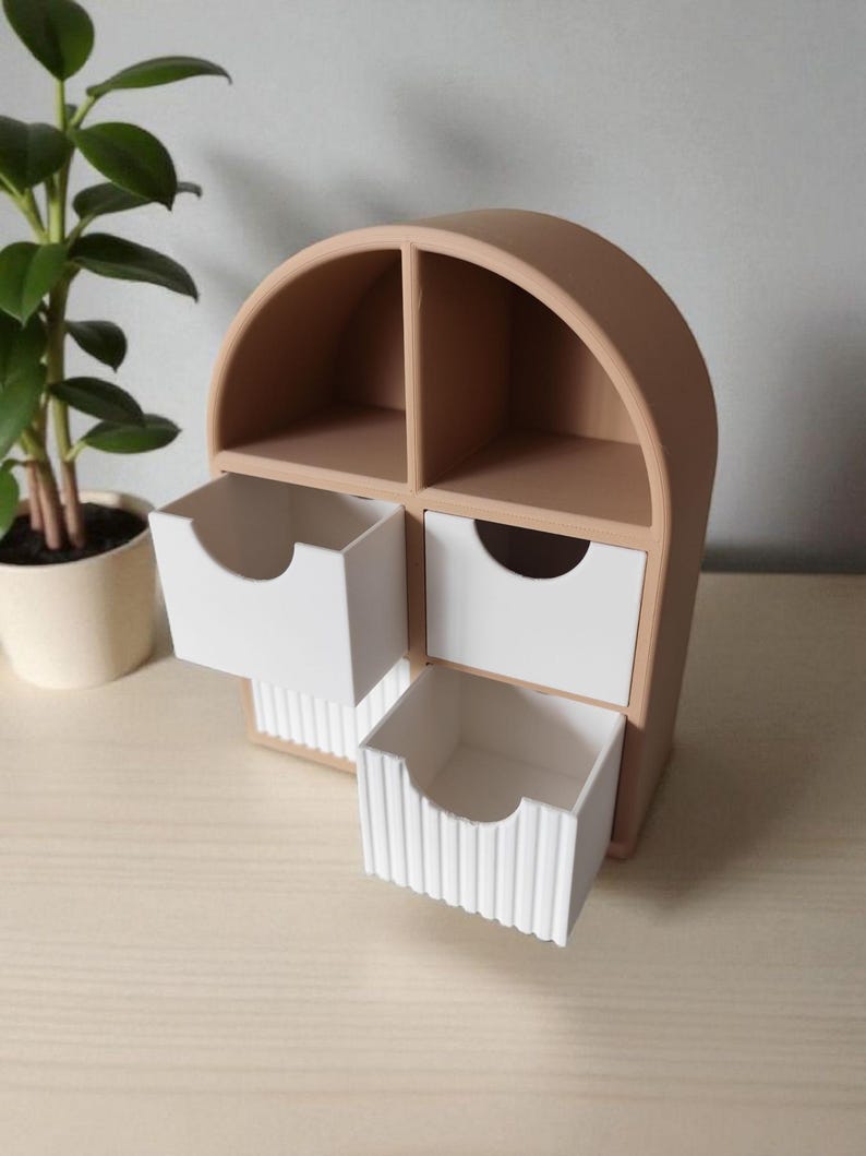 May include: A tan arched desktop organizer featuring four compartments. Two upper sections are open, while two lower sections contain white drawers. The bottom drawer has a vertical ribbed texture on its front face, and both drawers feature a circular cutout.