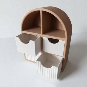 May include: A tan arched desktop organizer featuring two open upper compartments and two white drawers. The bottom drawer has a vertical ribbed texture on its front, while both drawers feature a semi-circular cutout for easy opening and access.