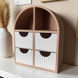 May include: A beige arched desktop organizer featuring two open top compartments and four drawers. The top two drawers have smooth white fronts, while the bottom two drawers feature a vertical ribbed texture. Each drawer has a semi-circular cutout.
