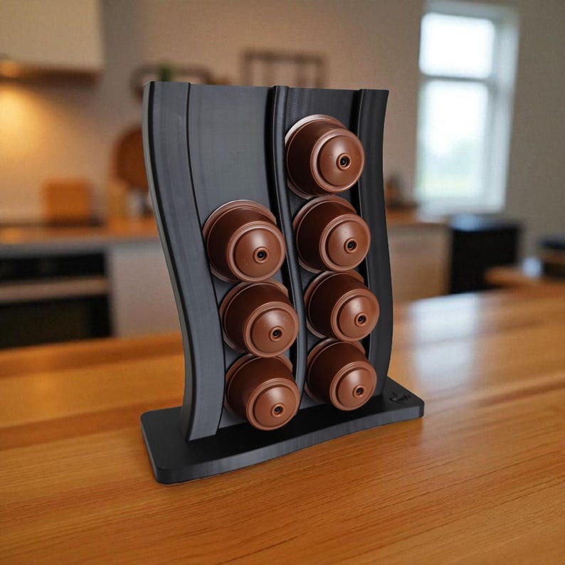 Puede incluir: Un soporte vertical negro para c&aacute;psulas de caf&eacute; con dise&ntilde;o ondulado, que cuenta con dos columnas para un total de ocho c&aacute;psulas de caf&eacute; marrones. El soporte tiene una base rectangular plana y un acabado mate y liso.