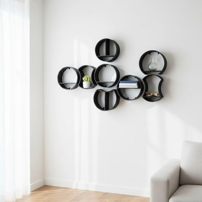 May include: A set of interconnected black circular wall shelves arranged in a cluster. The shelves feature various internal dividers and horizontal platforms, holding a small potted green plant, a clear glass vase, and a stack of books.