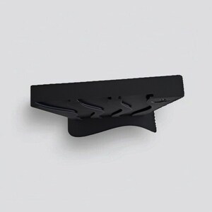 May include: A matte black rectangular stand featuring a series of three curved, wave-like indentations along its top surface. The object has a solid, angled base that provides support, creating a distinct silhouette against the plain background.