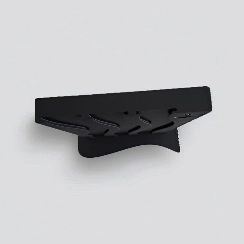 May include: A matte black rectangular stand featuring a series of three curved, wave-like indentations along its top surface. The object has a solid, angled base that provides support, creating a distinct silhouette against the plain background.