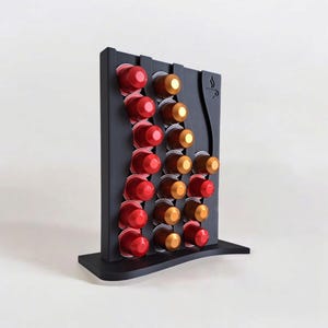 May include: A black vertical coffee pod holder with a wavy design, featuring three columns of slots filled with red and gold coffee capsules. The stand has a flat base and a small coffee cup icon engraved on the upper right side of the frame.