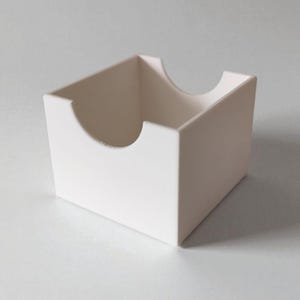 May include: A matte white square storage box with an open top and a semi-circular cutout on the front and back panels. The container features clean, straight edges and a smooth, uniform finish, providing an open design for easy access to contents.