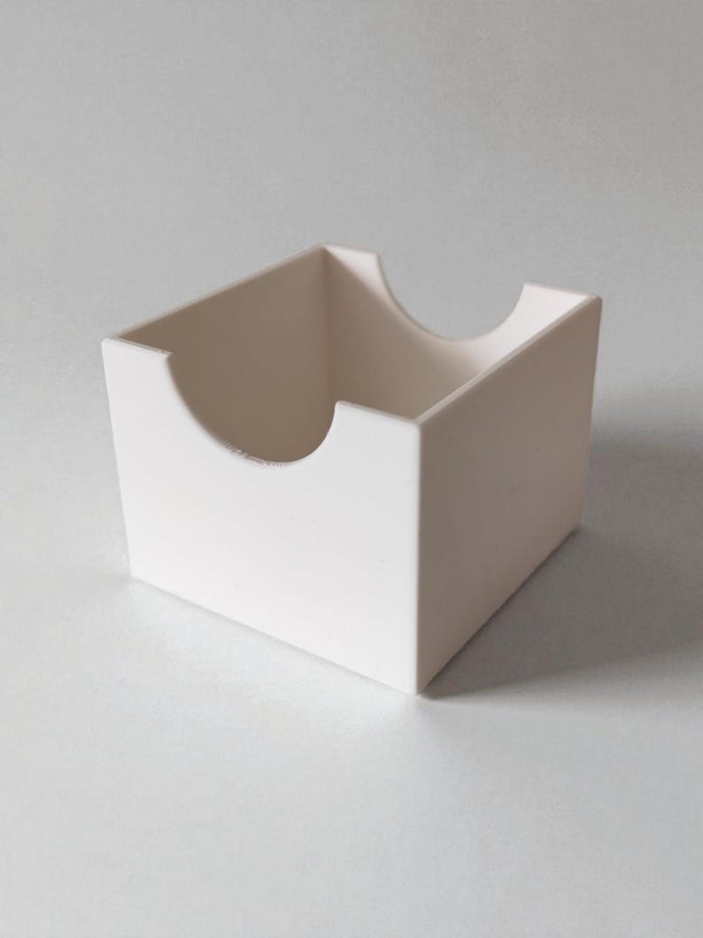 May include: A matte white square storage box with an open top and a semi-circular cutout on the front and back panels. The container features clean, straight edges and a smooth, uniform finish, providing an open design for easy access to contents.