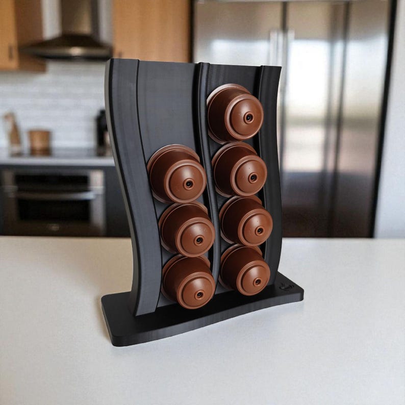 Puede incluir: Un soporte vertical negro para c&aacute;psulas de caf&eacute; con dise&ntilde;o ondulado, que cuenta con dos columnas para un total de ocho c&aacute;psulas de caf&eacute; marrones. El soporte tiene una base rectangular plana y un acabado mate y liso.