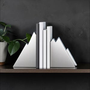Peut inclure: Une paire de serre-livres en m&eacute;tal argent&eacute; en forme de sommets de montagne, maintenant trois livres &agrave; la verticale. Les serre-livres pr&eacute;sentent une finition m&eacute;tallique bross&eacute;e avec des silhouettes triangulaires angulaires.
