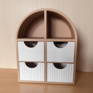 May include: A beige arched desktop organizer featuring two open top compartments and four drawers. The two upper drawers are smooth white, while the two lower drawers feature a vertical ribbed texture, each with a semi-circular cutout handle.