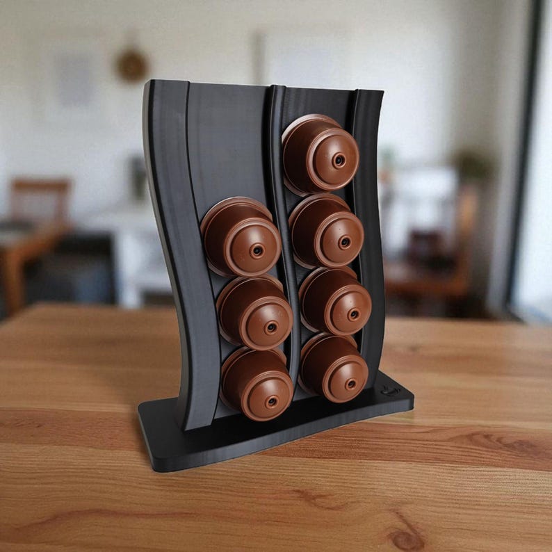 Puede incluir: Un soporte vertical negro para c&aacute;psulas de caf&eacute; con dise&ntilde;o ondulado, que cuenta con dos columnas para un total de ocho c&aacute;psulas de caf&eacute; marrones. El soporte tiene una base rectangular plana y un acabado liso y mate en toda su estructura.