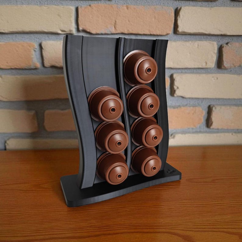 Puede incluir: Un soporte vertical negro para c&aacute;psulas de caf&eacute; con dise&ntilde;o ondulado, que cuenta con dos columnas para albergar un total de ocho c&aacute;psulas de caf&eacute; marrones. El soporte tiene una base plana y un acabado mate liso para organizar c&aacute;psulas.