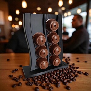 Puede incluir: Un soporte vertical negro para c&aacute;psulas de caf&eacute; con dise&ntilde;o ondulado, que cuenta con dos columnas para un total de ocho c&aacute;psulas de caf&eacute; marrones. El soporte est&aacute; colocado en posici&oacute;n vertical sobre una superficie plana con granos de caf&eacute;.
