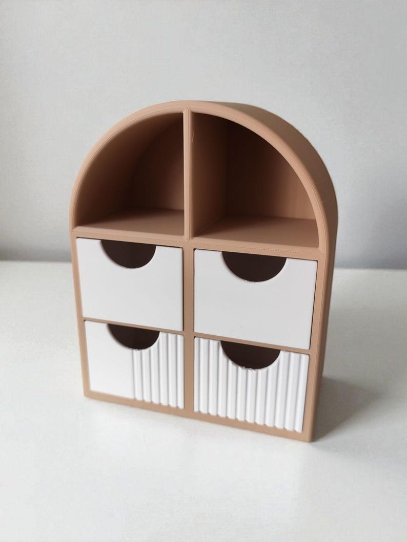 May include: A tan desktop organizer with an arched top, featuring two open upper compartments and four lower drawers. The two bottom drawers have a vertical ribbed texture on their white faces, while the two top drawers are smooth white.