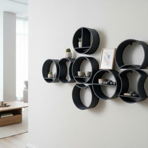 May include: A collection of matte black circular wall shelves arranged in a cluster. The shelves feature various internal dividers and horizontal surfaces holding small potted succulents, ceramic bowls, smooth stones, and a framed picture.