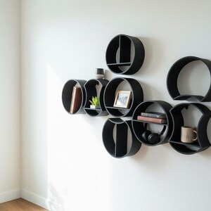 May include: A collection of black circular wall shelves arranged in a cluster. The shelves feature various internal dividers and flat surfaces for storage, holding items such as books, a small potted plant, a picture frame, and a ceramic mug.