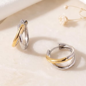 May include: A pair of small hoop earrings featuring a two-tone design. Each earring consists of a polished silver-tone metal hoop accented with a smooth, curved gold-tone metal segment that overlays the front portion of the circular band.