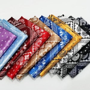 May include: A collection of folded square fabric bandanas featuring a classic paisley pattern. The set includes various colors such as purple, light blue, dark red, bright red, tan, royal blue, gold, white, and black, all with white detailing.