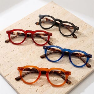 May include: Four pairs of round-frame glasses with clear lenses. The frames feature a matte finish in black, red, blue, and orange, each paired with brown and black tortoiseshell patterned temples. The glasses are arranged in a staggered formation.