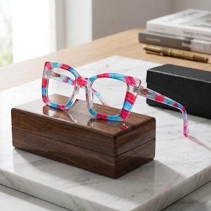 May include: Square-framed eyeglasses featuring a translucent acetate material with a vibrant, multi-colored pattern of bright pink, light blue, and white swirls. The frames have clear lenses and integrated nose pads, showcasing a bold, colorful aesthetic.