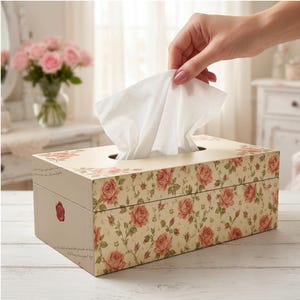 Peut inclure: Une boîte à mouchoirs rectangulaire avec une base de couleur crème ornée d'un motif répétitif de roses roses et de feuilles vertes. La boîte présente un emblème de sceau en cire rouge sur le côté et un mouchoir blanc sortant par l'ouverture.
