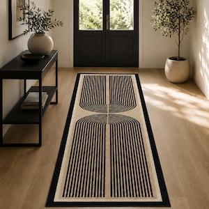 May include: A rectangular runner rug featuring a beige background with a bold black geometric pattern of two mirrored arch shapes composed of parallel vertical lines. The rug has a solid black border framing the entire design on a wooden floor.