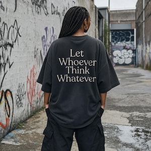 Pode incluir: Uma t-shirt cinzento-carvão de corte oversize com o texto branco Let Whoever Think Whatever estampado nas costas. A peça tem mangas curtas, decote redondo e um ajuste descontraído, vista de costas com as mãos nos bolsos.