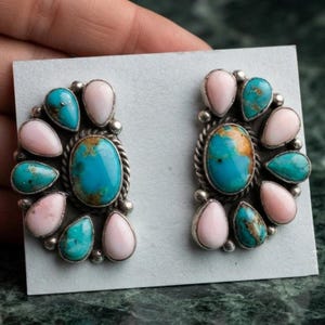 Könnte beinhalten: Ein Paar silberne Ohrringe mit einem zentralen ovalen Türkis, umgeben von abwechselnd tropfenförmigen rosa Steinen und kleineren Türkisen. Die Metallfassungen sind mit gedrehten Kordeldetails und kleinen Silberperlen verziert.
