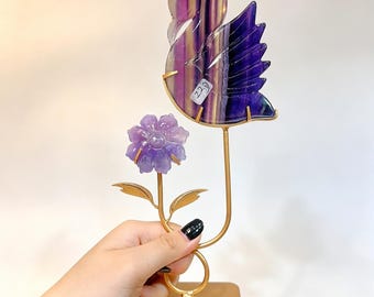 Könnte beinhalten: Ein dekoratives Ornament mit einem geschnitzten Schwan aus violettem und gelbem Fluorit und einer hellvioletten geschnitzten Blume auf einem goldfarbenen Metallständer. Der Schwan hat einen kleinen weißen Aufkleber mit dem Text 220.