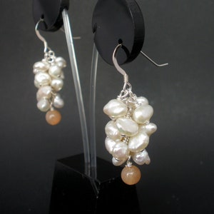 May include: A pair of silver earrings with a cluster of white pearls and a peach-colored gemstone dangling from each earring.