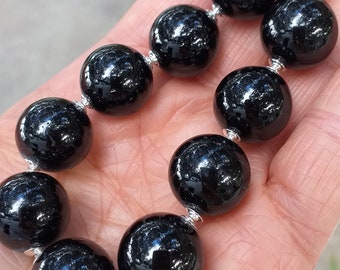 Può includere: Un braccialetto nero con perline e connettori argentati. Le perline sono rotonde e hanno una superficie lucida e riflettente.